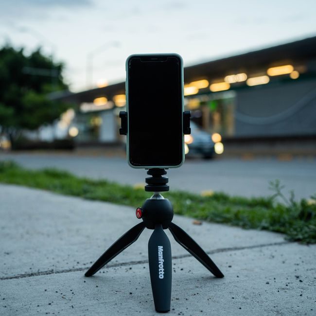 Smartphone on a tripod on a sidewalk captures a city scene at dusk, highlighting portability and technology. — Amar  Preciado, Pexels