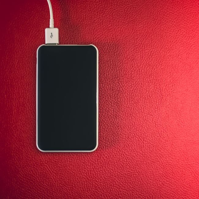 A smartphone connected to a charger placed on a red leather surface. — Steve A Johnson, Pexels