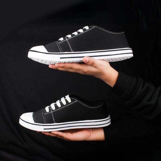 Pair of black sneakers held in hands against a dark background, showcasing minimalist fashion footwear. — ALOK DAS, Pexels