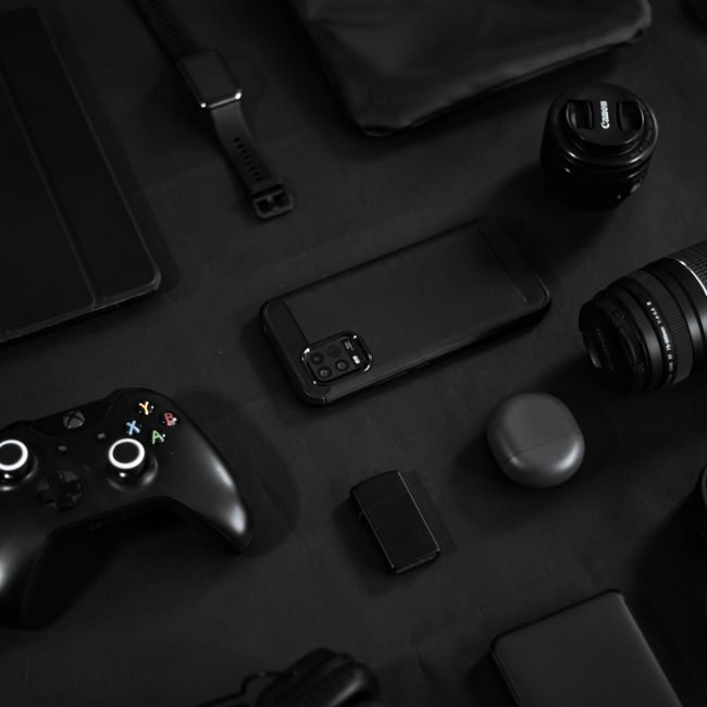 Stylish arrangement of gadgets including a smartphone, lens, and game controller on a black surface. — Carlos Jairo, Pexels
