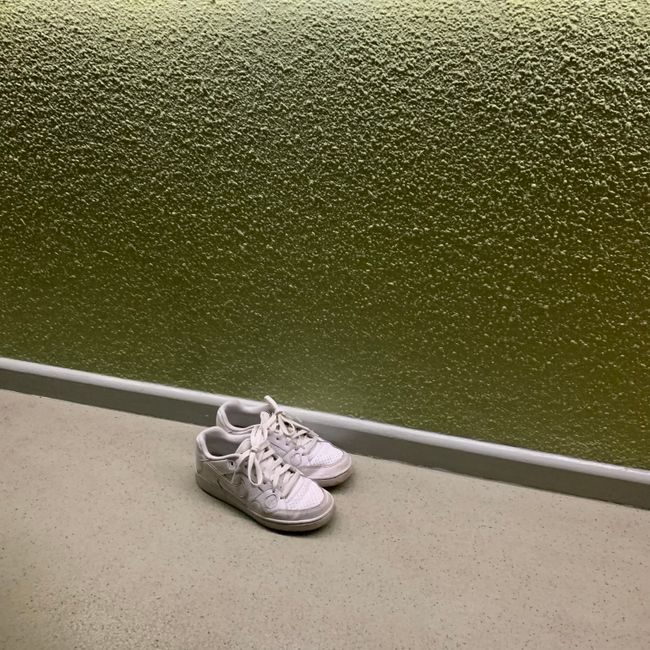 Pair of white sneakers against a textured olive green wall in a minimalist setting, perfect for fashion or lifestyle themes. — Clarisse Vidal, Pexels