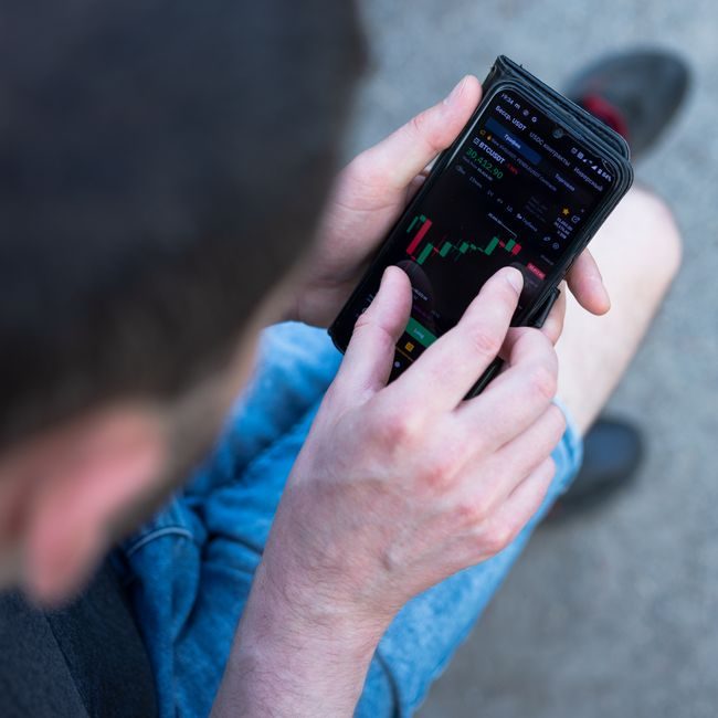 A man in casual attire checks cryptocurrency prices on his smartphone outdoors. — Karyna Panchenko, Pexels