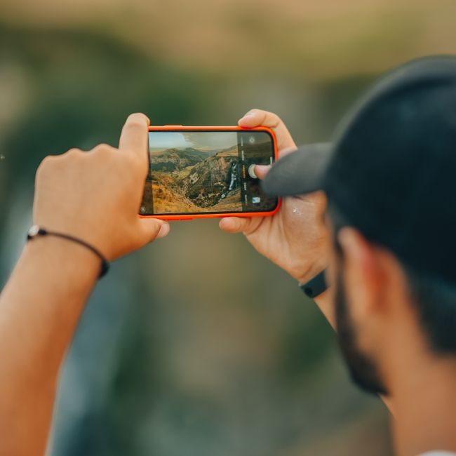 A man using a smartphone to photograph a scenic mountain view in Kars, Türkiye. — Berkay AK, Pexels