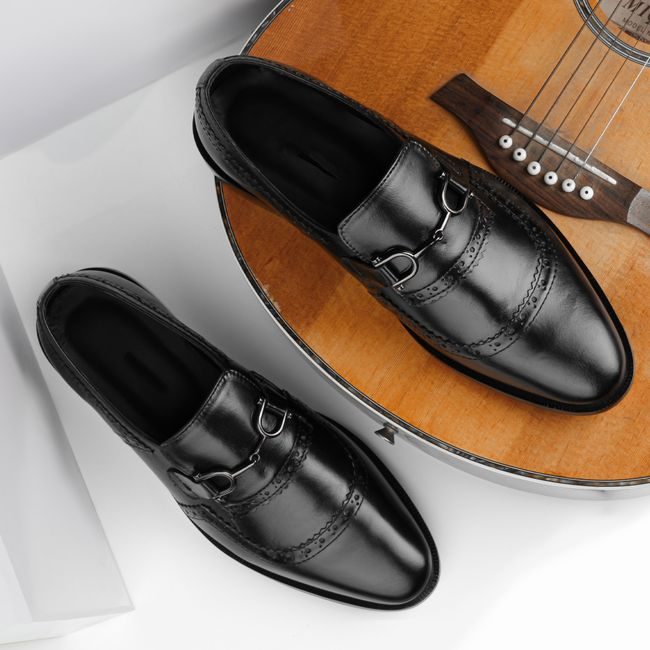 Elegant black leather loafers displayed on an acoustic guitar in a modern composition. — Danyal Malik, Pexels