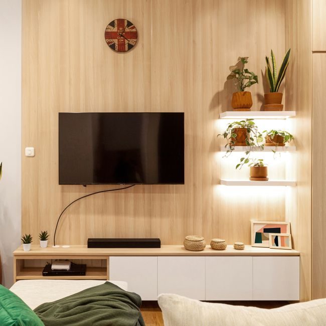 Cozy living room featuring a wall-mounted TV, wooden shelves, and potted plants. — Hakim  Santoso, Pexels