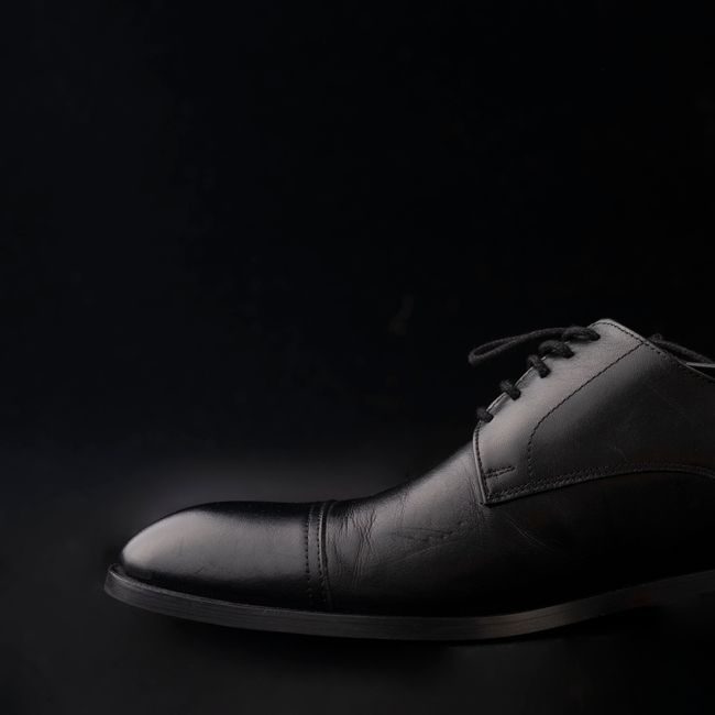 Detailed close-up of a classic black leather Oxford shoe against a dark background. — Ali Nafezarefi, Pexels