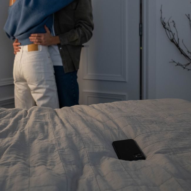 Couple embracing in a cozy bedroom with a smartphone lying on the bed. — Ron Lach, Pexels