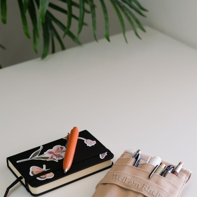 A clean minimalist workspace featuring a decorated notebook and a pen holder on a white desk. — Zeynep  Hız, Pexels