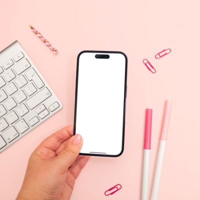 A minimalistic pink-themed workspace showcasing a smartphone mockup held in hand. — Jilly Noble, Pexels