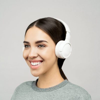 Close-up of a smiling young woman with headphones, wearing casual attire in a studio setting. — Sound On, Pexels