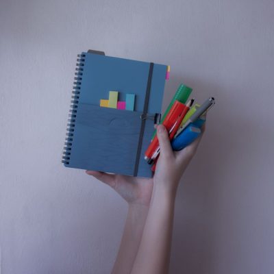 A person holding a notebook with colorful pens and sticky notes, showcasing stationery organization. — Alexandra Krainyukhova, Pexels