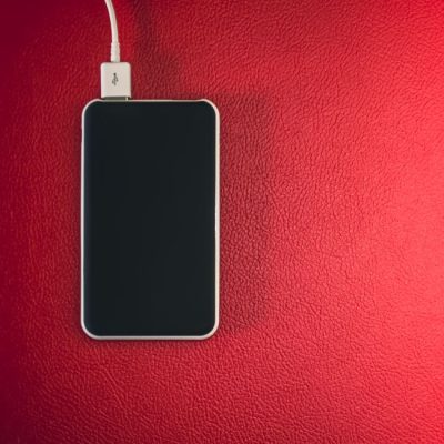 A smartphone connected to a charger placed on a red leather surface. — Steve A Johnson, Pexels