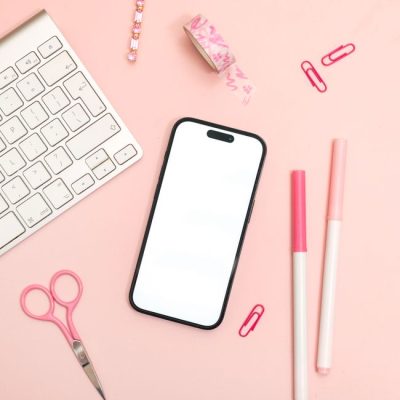 Flat lay of a pink themed office desk setup with an iPhone, keyboard, and stationery. — Jilly Noble, Pexels
