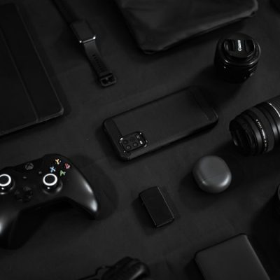 Stylish arrangement of gadgets including a smartphone, lens, and game controller on a black surface. — Carlos Jairo, Pexels