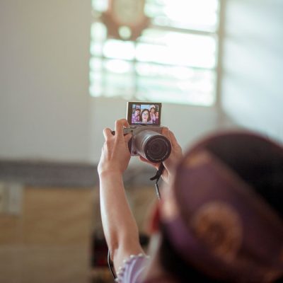 A person taking a selfie indoors using a DSLR camera, with sunlight streaming through a window. — Min An, Pexels