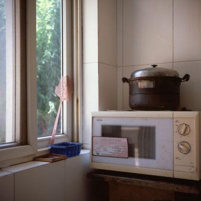 Sunlit kitchen corner with a microwave, vintage pot, and window view. — Zechen Li, Pexels
