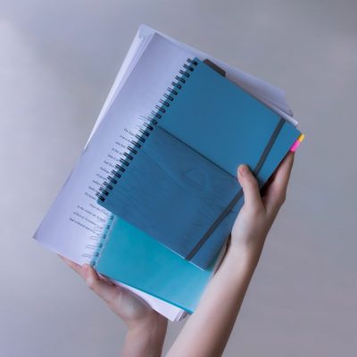 Hands hold blue spiral-bound notebooks and papers, showcasing organization and study. — Alexandra Krainyukhova, Pexels