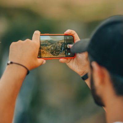 A man using a smartphone to photograph a scenic mountain view in Kars, Türkiye. — Berkay AK, Pexels