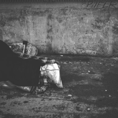 Black and white image of a person sleeping on the sidewalk, depicting urban hardship. — Taufiq Klinkenborg, Pexels