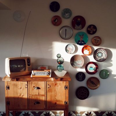 Retro living room setup featuring a vintage TV, typewriter, and decorative wall plates, bathed in warm daylight. — Fatma K.duman, Pexels