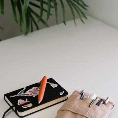 A clean minimalist workspace featuring a decorated notebook and a pen holder on a white desk. — Zeynep  Hız, Pexels